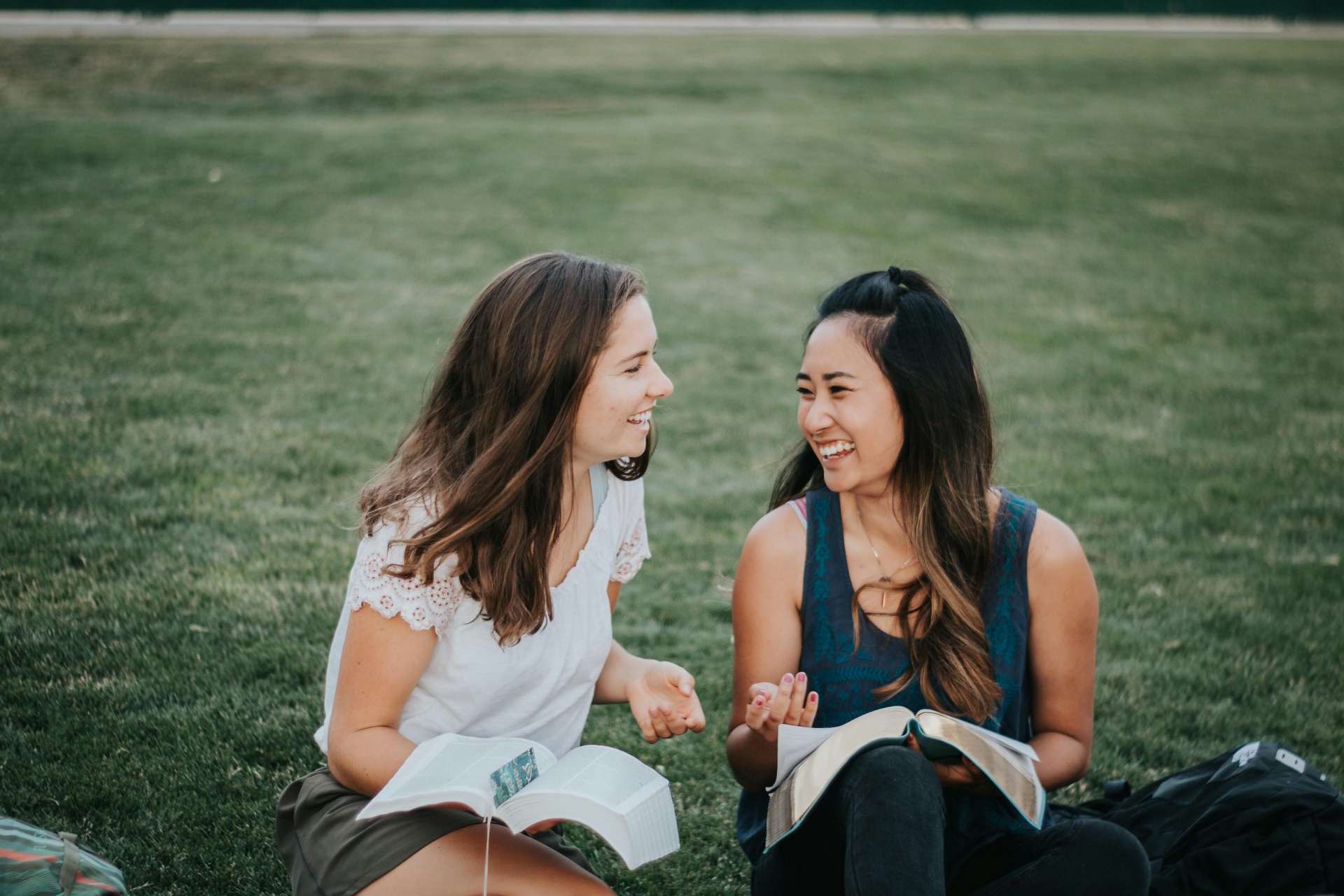 Two women laughing as they study the Bible together outdoors